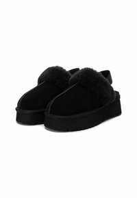 Zapatos de plataforma negros tipo slip-on con un grueso forro de piel sintética y una correa elástica en la parte trasera, diseñados para brindar calidez y comodidad.
