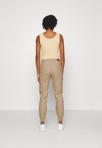 Débardeur beige à encolure dégagée, associé à un pantalon cargo khaki avec poches latérales et poignets élastiques, complété par des baskets blanches.