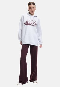 Szary, oversize'owy hoodie z grafiką "Manhattan", zestawiony z burgundowymi spodniami w dzwony. Gładki materiał o luźnym kroju i minimalistycznym designie.