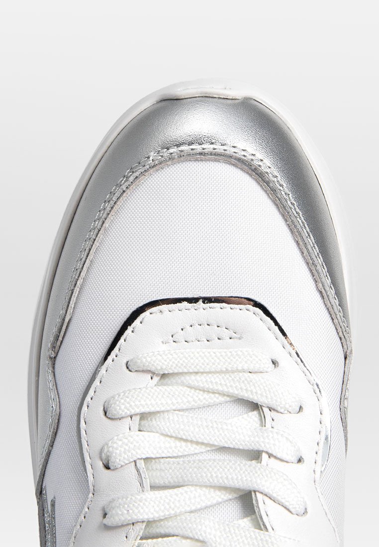 Baskets blanches avec un embout métallisé argenté, un dessus texturé et des lacets blancs. Présente des détails de branding minimalistes sur le côté.