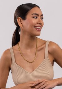 Goldfarbene, gedrehte Kettenhalskette, die über einem beige gerippten Oberteil getragen wird; glatte Textur mit glänzender Oberfläche, klassisches Design und nahtlose Glieder.