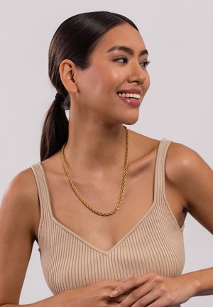 Collier en chaîne torsadée dorée porté sur un haut beige à côtes ; texture lisse avec une finition brillante, présentant un design classique et des maillons sans couture.