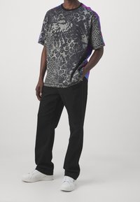 Grafisk t-shirt med ett svart och grått djurmönster, med lila detaljer på axlarna; matchas med svarta byxor och vita sneakers.