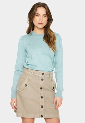 Lichtblauwe trui met ronde hals en lange mouwen, gecombineerd met een beige rok met een voorknopsluiting en twee zijzakken.