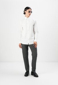 White long-sleeve button-up shirt, gray tailored pants, and black leather shoes. The sunglasses are round with a metallic frame.