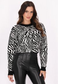 Melnās un baltās zebra svītrās apgrieztais džemperis no mīksta auduma, ar garām piedurknēm un apaļu kakla izgriezumu. Valkāts ar augsta vidukļa melnām biksēm.