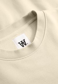 Beige sweatshirt met een geribde ronde hals en een stoffen label met een gestileerd logo. Glad materiaal, minimalistisch ontwerp.