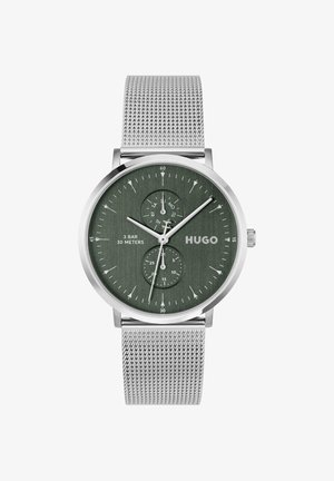 Montre à bracelet en maille argentée avec cadran vert foncé, aiguilles argentées, deux sous-cadrans pour le jour et les secondes, et logo "HUGO" sur le côté droit.