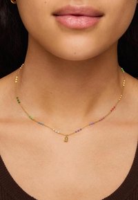 Collar de cadena de oro con acentos de cuentas multicolores, que presenta un pequeño charm. Diseño ligero y delicado, adecuado para superponer.
