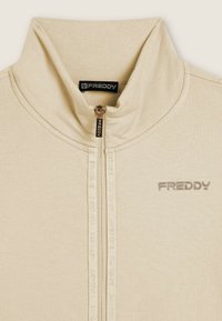 Giacca zip-up beige con alto colletto, logo Freddy grigio sul petto, dettaglio della zip testurizzato e tessuto morbido. Design semplice e pulito.