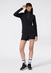 Black athletic top with a quarter-zip and "Champion" logo, paired with black shorts, white socks with stripes, and black sneakers.