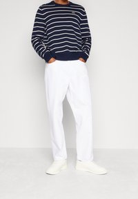 Pull en maille à rayures marines avec des lignes horizontales blanches, poignets et ourlet côtelés. Associé à un pantalon blanc à jambes droites et des baskets blanches.