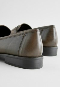 Pantofi din piele maro cu o textură netedă, design cu profil redus și o talpă solidă din cauciuc negru; cusături vizibile pe laterale.