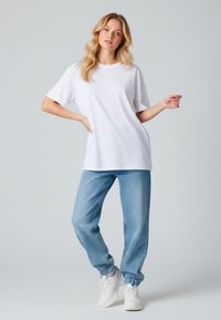 Witte T-shirt met korte mouwen in combinatie met lichtblauwe, loszittende jeans en witte sneakers. Het T-shirt heeft een ronde halslijn en een relaxte pasvorm.