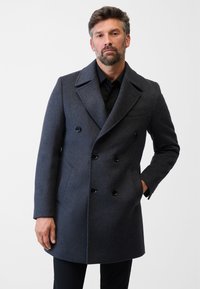 Mørkegrå uld peacoat med dobbeltknaplukning, store sorte knapper og sidelommer. Har en slå-om krave og tætsiddende pasform.