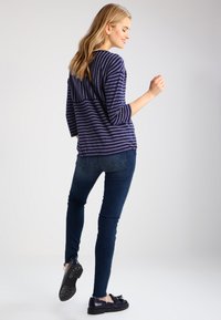 Top de rayas navy y blanco de manga larga, combinado con jeans skinny de mezclilla oscura y zapatos negros, visto desde atrás con un ligero giro.