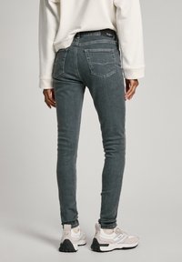 Jeans grises ajustados con una textura desgastada, dos bolsillos traseros y costuras en contraste, combinados con zapatillas blancas y grises.
