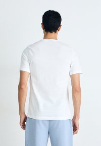 T-shirt en coton blanc à manches courtes, col rond et texture lisse. L'arrière est uni, sans motifs ni détails visibles.