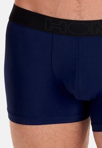 Marineblauwe boxershorts van glad materiaal, met een zwart elastieken tailleband met merk en een aansluitend ontwerp.