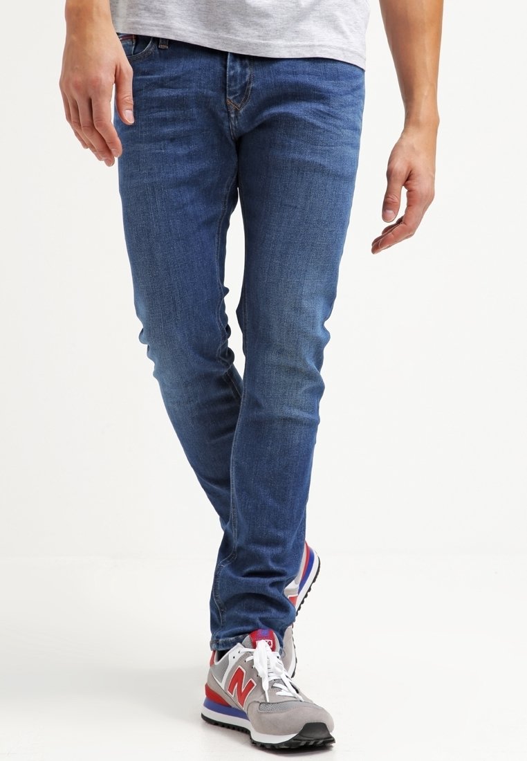 Blå denimjeans med slim fit, som visar en mjuk textur och minimal sömnad, tillsammans med grå och röda sportskor.