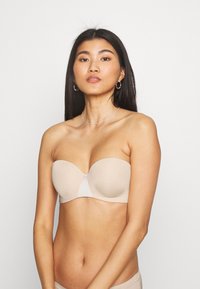Beige strapless bra with smooth fabric, molded cups, and a sheer center panel. Simple, rounded design with minimal hardware.