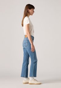 T-shirt blanc à manches courtes avec impression graphique, associé à un jean taille haute bleu clair et des baskets blanches avec des accents texturés.