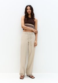Pantalons beiges à jambes larges avec taille à cordon, associés à un top court rayé marron et beige. Tissu texturé avec une finition lisse.