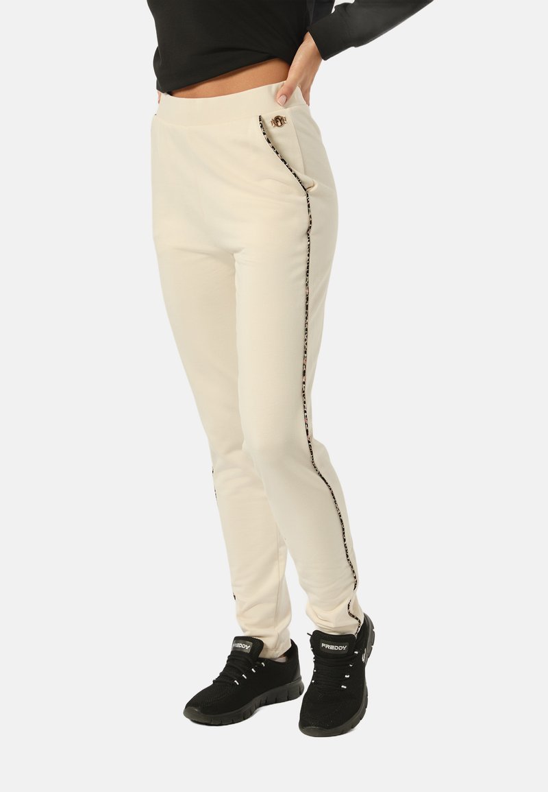 Pantalones jogger color crema con un corte ajustado, que cuentan con bolsillos laterales, acentos de estampado de leopardo negro y un logotipo dorado decorativo en la cintura.