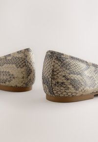 Beezhvärvi ja halli värvi madala kontsaga jalanõud, millel on maodermimuster, ümarad kontsad ja pruunid tallad heledal taustal.