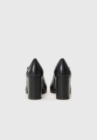 Schwarze Leder high-heeled Schuhe mit spitzem Zehenbereich und breitem Blockabsatz, ausgestattet mit einer glatten Textur und minimalistischem Design.