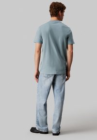 Camiseta de algodón de color azul claro con mangas cortas, cuello redondo y aberturas laterales, combinada con jeans de mezclilla de lavado claro y zapatos negros.