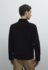 Polo shirt nero a maniche lunghe in un tessuto morbido, con colletto e una texture liscia, mostrato da una vista posteriore, con una vestibilità comoda.