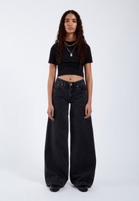 Black cropped t-shirt paired with wide-leg black denim jeans. The jeans feature a classic five-pocket design and metallic hardware.