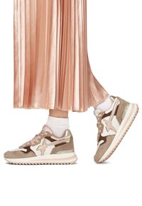 Zapatillas con un upper de ante beige, acentos en rosa claro, paneles blancos y una suela texturizada. Combinadas con una falda de satén plisada.