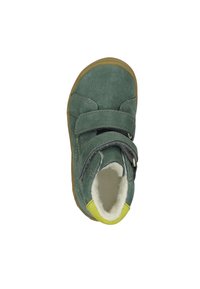 Grüner Wildlederschuh mit einem Klettverschluss, kontrastierendem gelben Akzent am Absatz und einem weichen weißen Futter innen. Runde Zehenform.