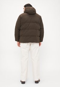 Brun polstret jakke med hætte, der har vandret syninger. Båret over off-white bukser, der viser en afslappet pasform og minimalistisk design.
