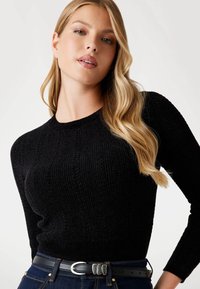 Maglione nero a coste con scollatura rotonda e maniche lunghe, abbinato a jeans di denim scuro e una cintura nera con fibbia argentata.