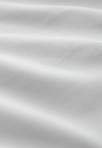 Tissu blanc lisse avec des plis doux et une texture agréable, visible sous un éclairage diffus.