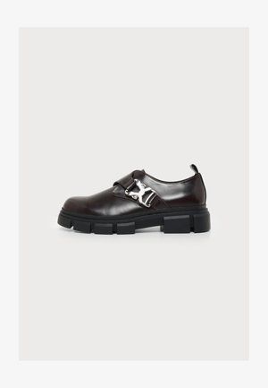 Tumepruunast nahast loafers paksu musta taldaga ja metallist pandla detailiga valgel taustal.