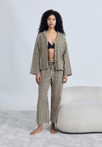 Σετ πιτζάμες με καρό μοτίβο σε μαύρο και μπεζ, με πουκάμισο με κουμπιά και παντελόνια με ελαστική μέση, διαθέτοντας άνετη εφαρμογή και μαλακή υφή.