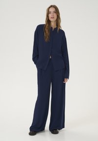 Completo due pezzi blu navy composto da una camicia a maniche lunghe con bottoni e pantaloni a gamba larga realizzati in un tessuto morbido e testurizzato.