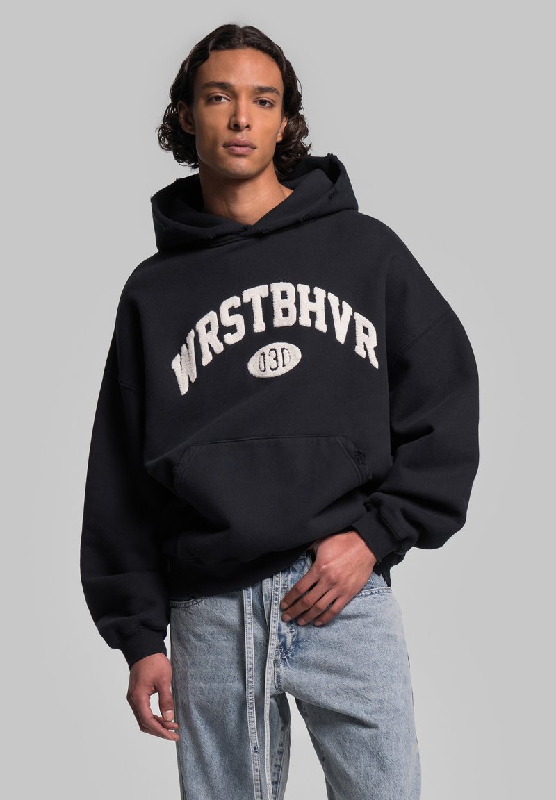 Felpa nera con la scritta "WRSTBHVR" e grafica di un pallone da football in lettere bianche, vestibilità oversize, tasca frontale, jeans in denim effetto morbido.