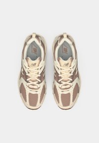 Light beige and brown mesh running shoes with textured overlays, padded collar, and flat laces. Features a "New Balance" logo on the tongue.