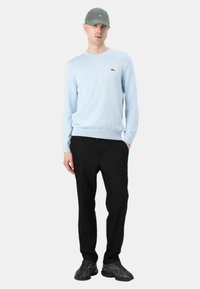 Hellblauer Strickpullover mit Rundhalsausschnitt, schwarze Hose und graue Mütze. Die Sneakers haben ein strukturiertes schwarzes Design. Einfaches, lässiges Outfit.