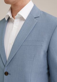 Helles blaues Blazer aus strukturiertem Stoff, mit einem Ein-Knopf-Verschluss, Reverskragen und einer Brusttasche auf der linken Seite.