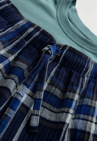 Teal-collinen t-paita pyöreällä kauluksella, yhdistettynä tummansinisiin ruudullisiin shortsit, joissa on naru vyötäröllä ja teksturoitu kangas.