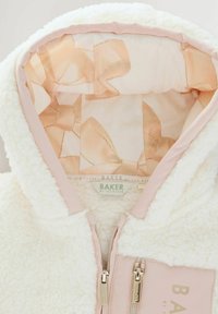 Felpa bianca in pile con fodera in satin rosa, caratterizzata da un motivo a fiocchi discreto. Include una chiusura con doppia zip e dettagli con patch del marchio.