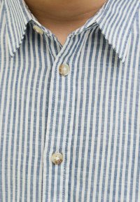 Camicia a righe blu e bianche con colletto button-down, due bottoni sulla patta e una finitura in tessuto testurizzato.