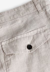 Pantaloni corti in lino di colore beige chiaro, dotati di una tasca posteriore chiusa con un bottone marrone scuro e dettagli cuciti.