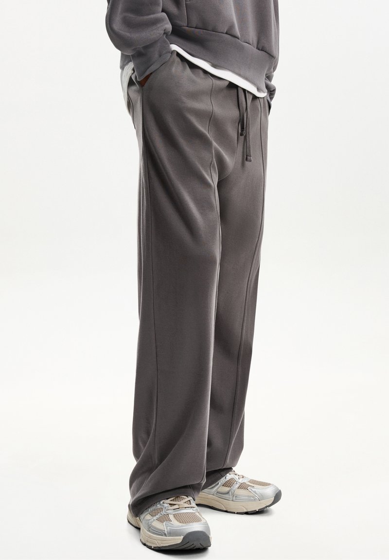 Grå, löst sittande sweatpants med elastisk midja och dragsko, med sidofickor och smidig textur. Åtföljs av ljusa sneakers.